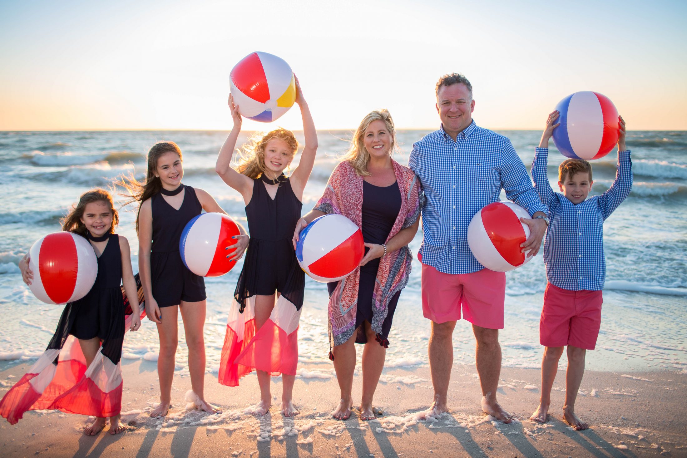 portraits family on the beach holding beach balls at sunset